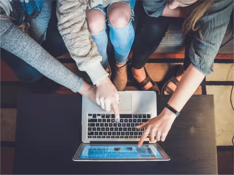 Three people sitting on a couch pointing at a laptop.